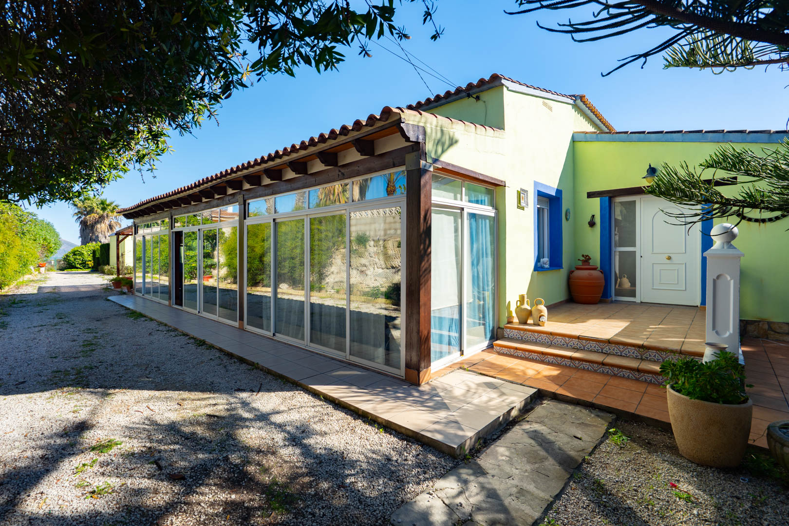 Extérieur de la finca avec une naya vitrée aux poutres en bois et un porche d'entrée carrelé aux accents bleus méditerranéens.
