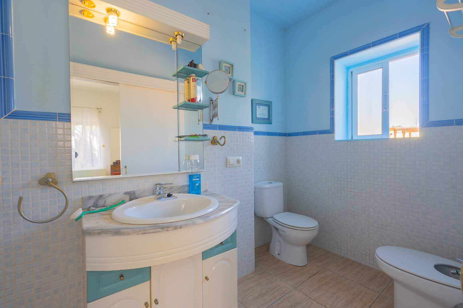 Salle de bains avec carrelage en mosaïque bleu et blanc, meuble vasque avec plan en marbre et éclairage naturel par une fenêtre latérale.