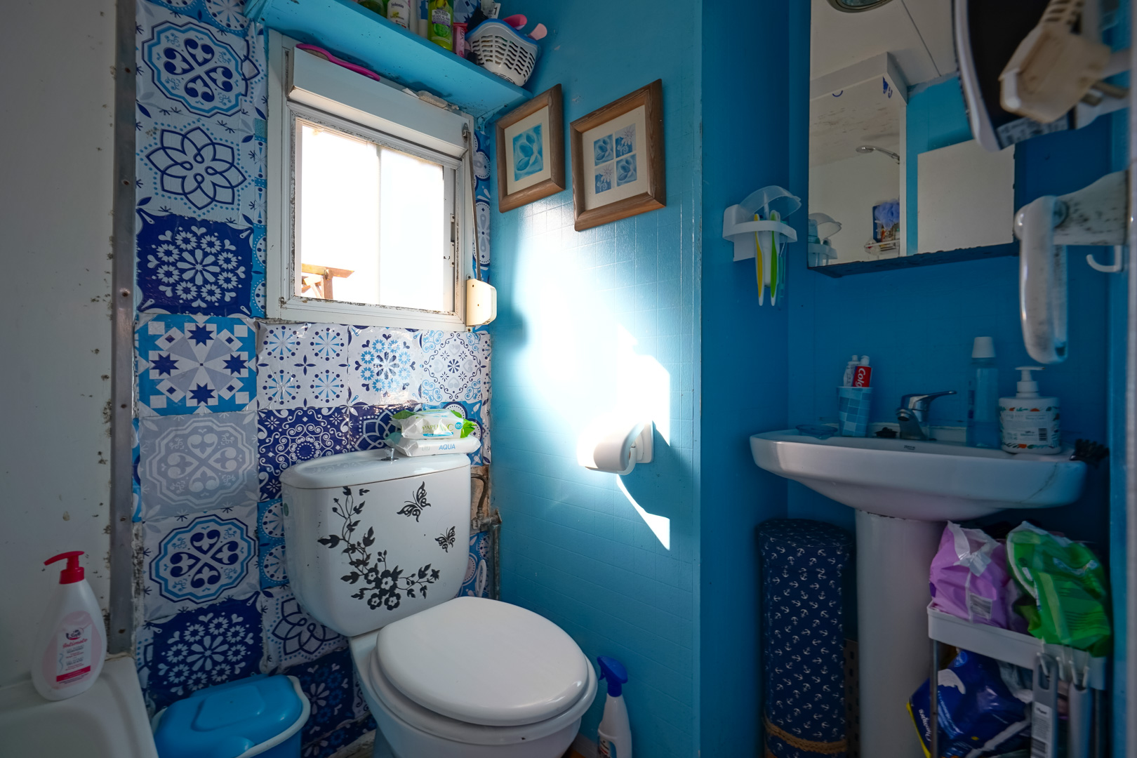 Salle d'eau compacte aux murs bleus, avec carrelage décoratif à motifs, lavabo sur colonne et fenêtre apportant une lumière naturelle.