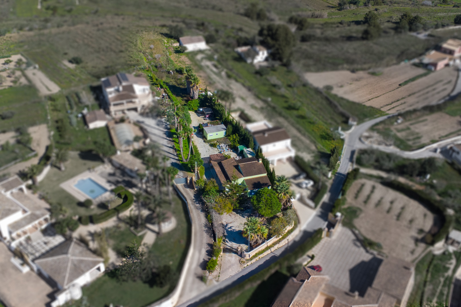 Vue aérienne de la parcelle rustique de 2 800 m2 montrant la villa principale, l'habitation préfabriquée et le terrain arboré de palmiers.