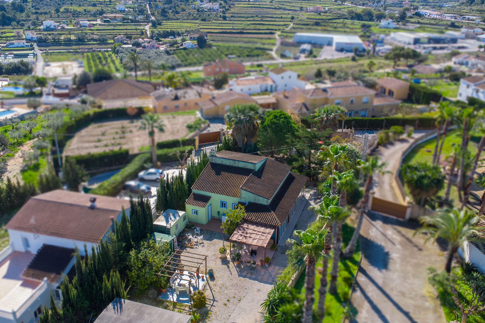 Vue aérienne de la propriété montrant la façade verte, les toits en tuiles et les espaces extérieurs aménagés avec pergolas et palmiers.