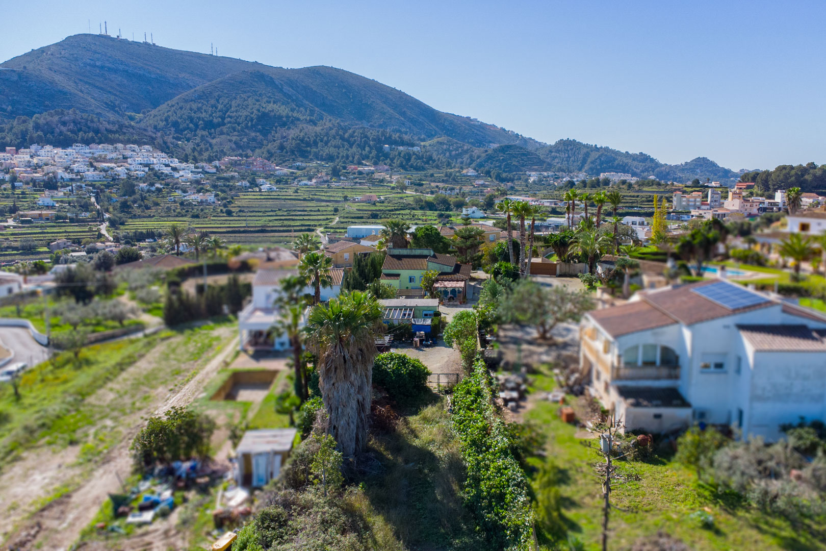Vue aérienne du terrain rustique avec la maison principale verte, l'unité préfabriquée et les vallées en terrasses avec vue sur la montagne.