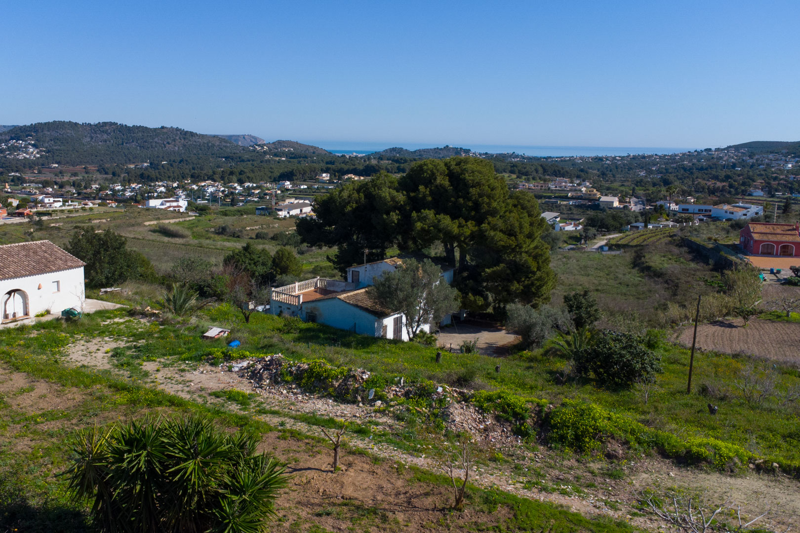 Vue surélevée de la finca traditionnelle et de son terrain rustique, offrant un panorama sur la vallée de Benitachell jusqu'à la mer Méditerranée.
