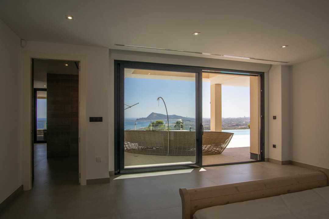 Chambre avec accès direct à la terrasse par des baies vitrées, offrant une vue dégagée sur la baie, les montagnes et le mobilier de jardin.