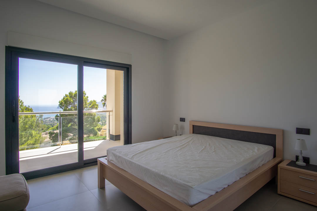 Chambre lumineuse avec cadre de lit en bois clair, accès direct à un balcon privé et vue dégagée sur le littoral méditerranéen et les pins environnants.