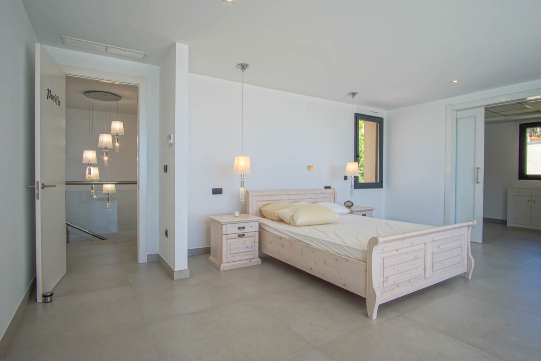 Chambre lumineuse avec cadre de lit en bois clair, tables de chevet assorties et suspensions. Comprend un sol en grès cérame gris et un accès à un dressing par porte coulissante.