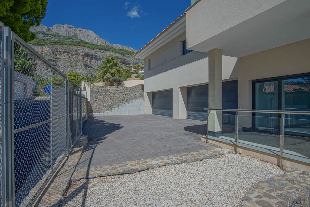 Entrée principale avec grand garage, murs en pierre naturelle et allée pavée offrant une vue sur les montagnes de la Sierra de Altea.