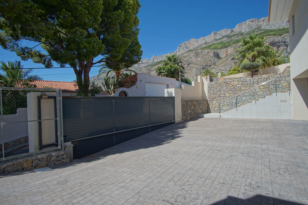 Entrée principale avec vaste allée en béton imprimé, portail coulissant sombre et murs en pierre naturelle avec vue sur la Sierra de Altea.
