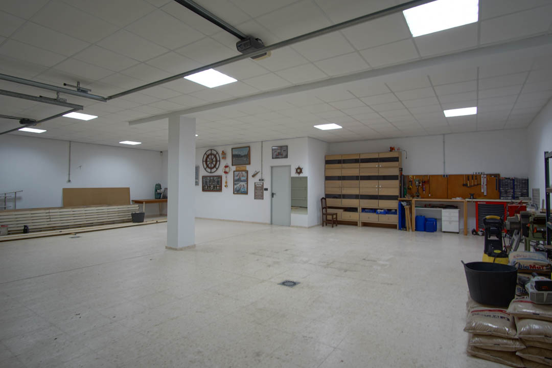 Garage spacieux pour plusieurs véhicules avec coin atelier, rangements intégrés, éclairage LED encastré et sol en grès facile d'entretien.
