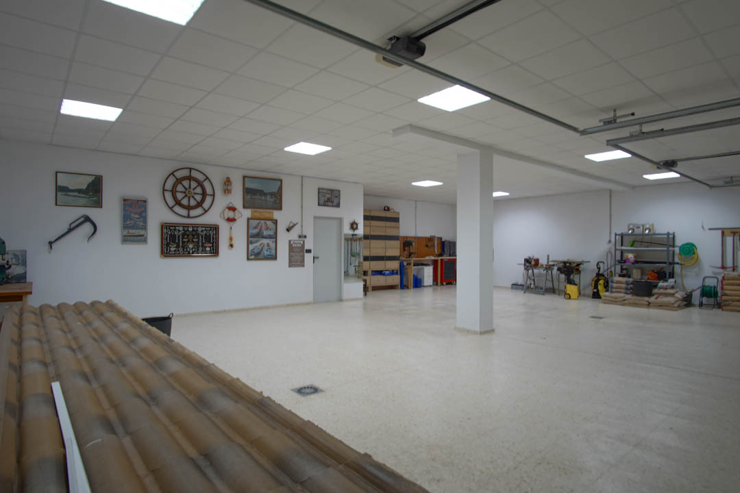 Grand garage pour cinq voitures avec éclairage LED encastré, espace atelier équipé et murs décorés d'éléments nautiques, offrant fonctionnalité et volume.