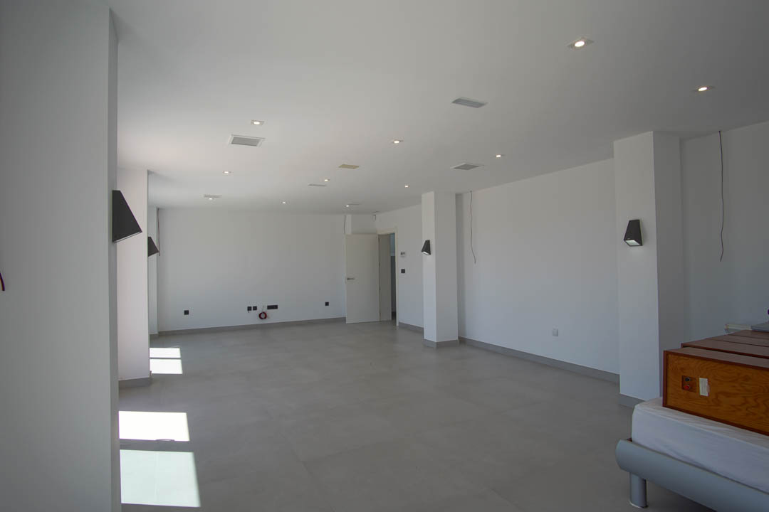 Grande pièce ouverte avec carrelage gris, murs blancs, spots encastrés au plafond et appliques murales au design moderne.