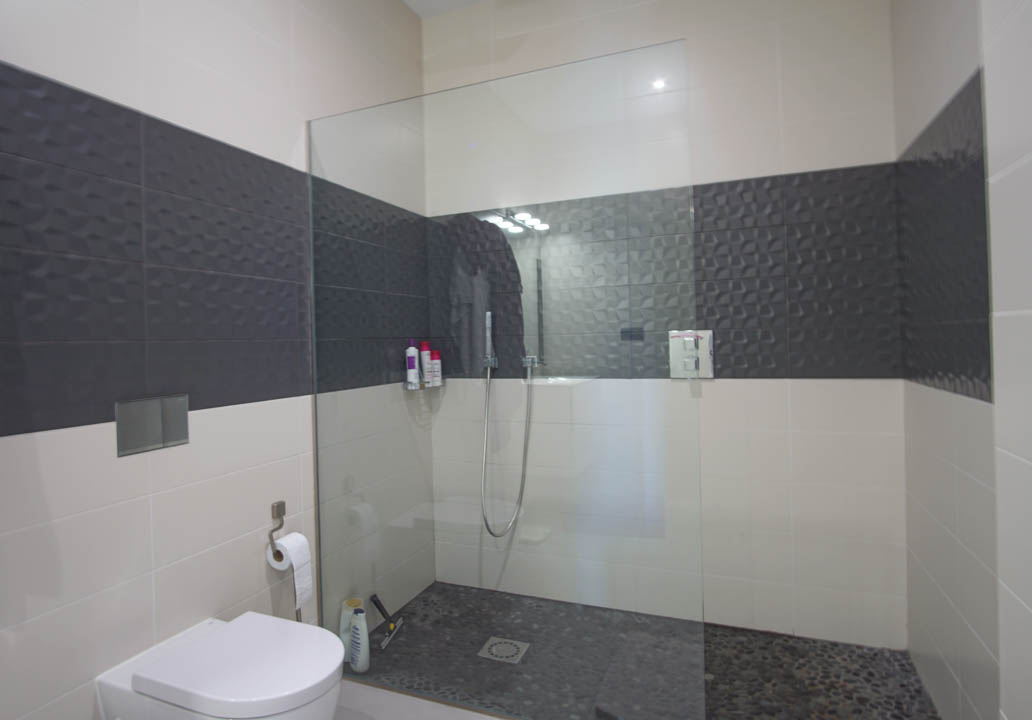 Salle de bains moderne avec douche à l'italienne, paroi en verre, sol en galets et carrelage mural texturé aux motifs géométriques.