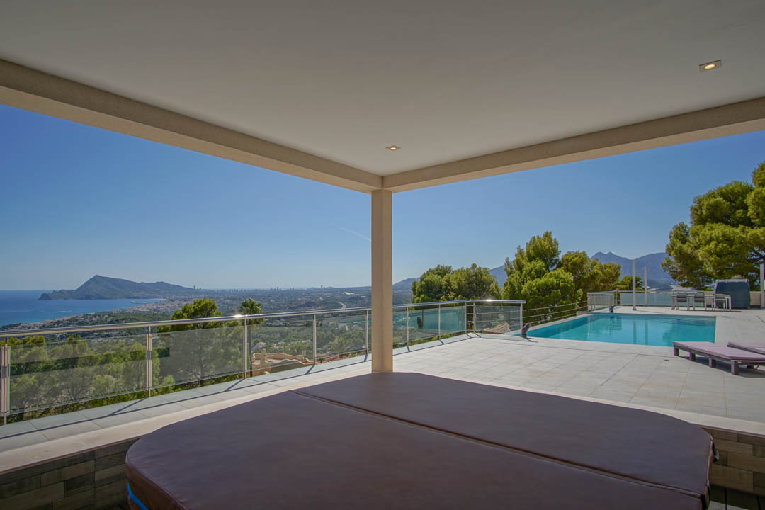 Terrasse couverte avec jacuzzi offrant une vue panoramique sur la baie d'Altea, complétée par une piscine extérieure et des garde-corps en verre.