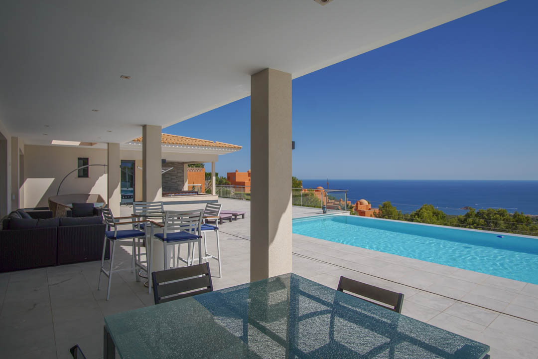 Terrasse couverte avec salon d'été et salle à manger, offrant une vue panoramique sur la mer Méditerranée et la piscine à débordement.