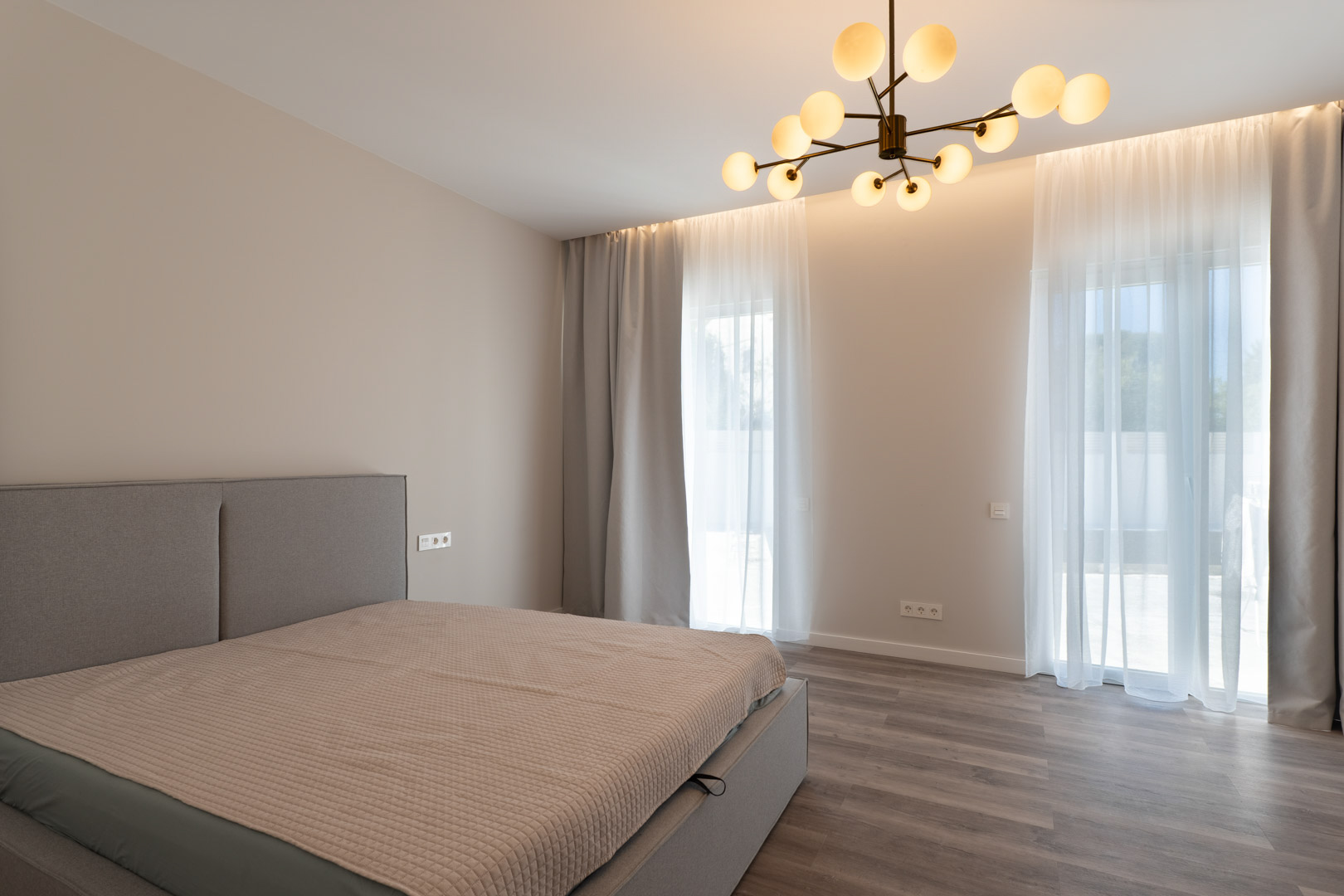 Chambre principale minimaliste avec parquet gris, éclairage LED indirect et un lustre contemporain à globes en verre dépoli.