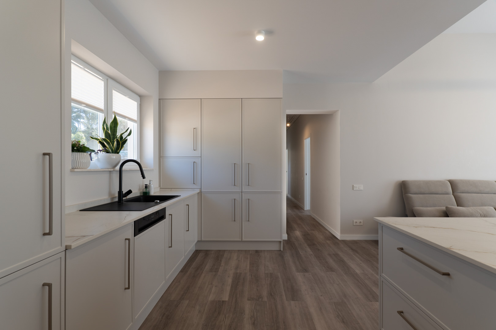 Cuisine minimaliste avec meubles blanc mat, plan de travail en pierre veinée et robinetterie noire. L'espace fonctionnel dispose d'un sol imitation bois et de lumière naturelle.