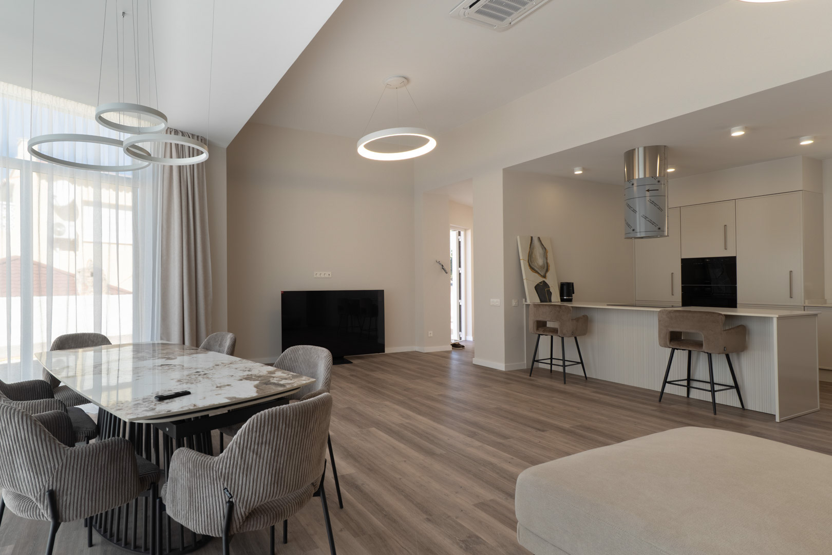 Espace de vie ouvert avec table en marbre, cuisine minimaliste intégrée et luminaires LED circulaires, le tout sur un sol en bois clair élégant.
