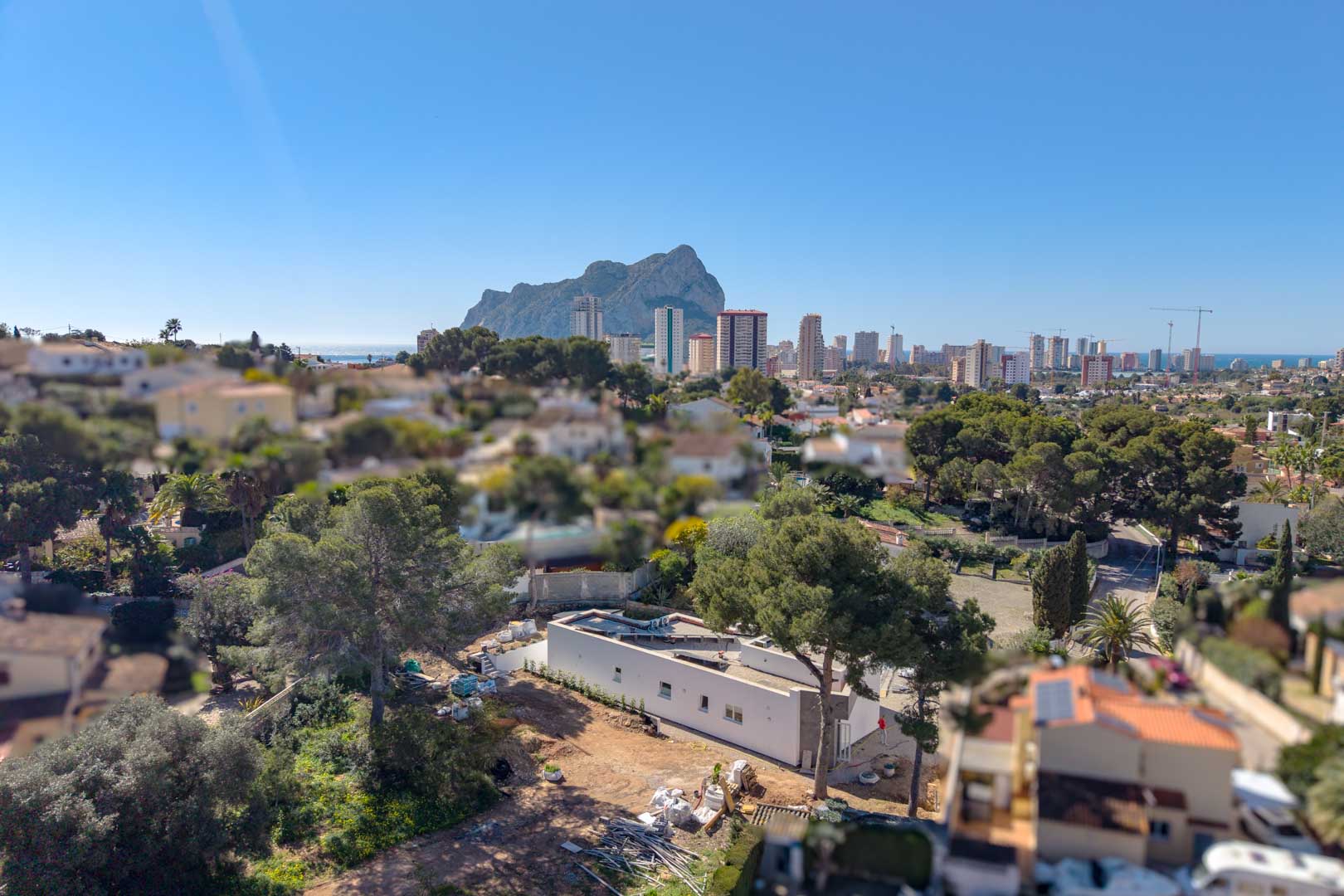 Perspective aérienne de la villa minimaliste en construction, soulignant son architecture de plain-pied et sa vue imprenable sur le Peñón de Ifach et l'horizon de Calpe.