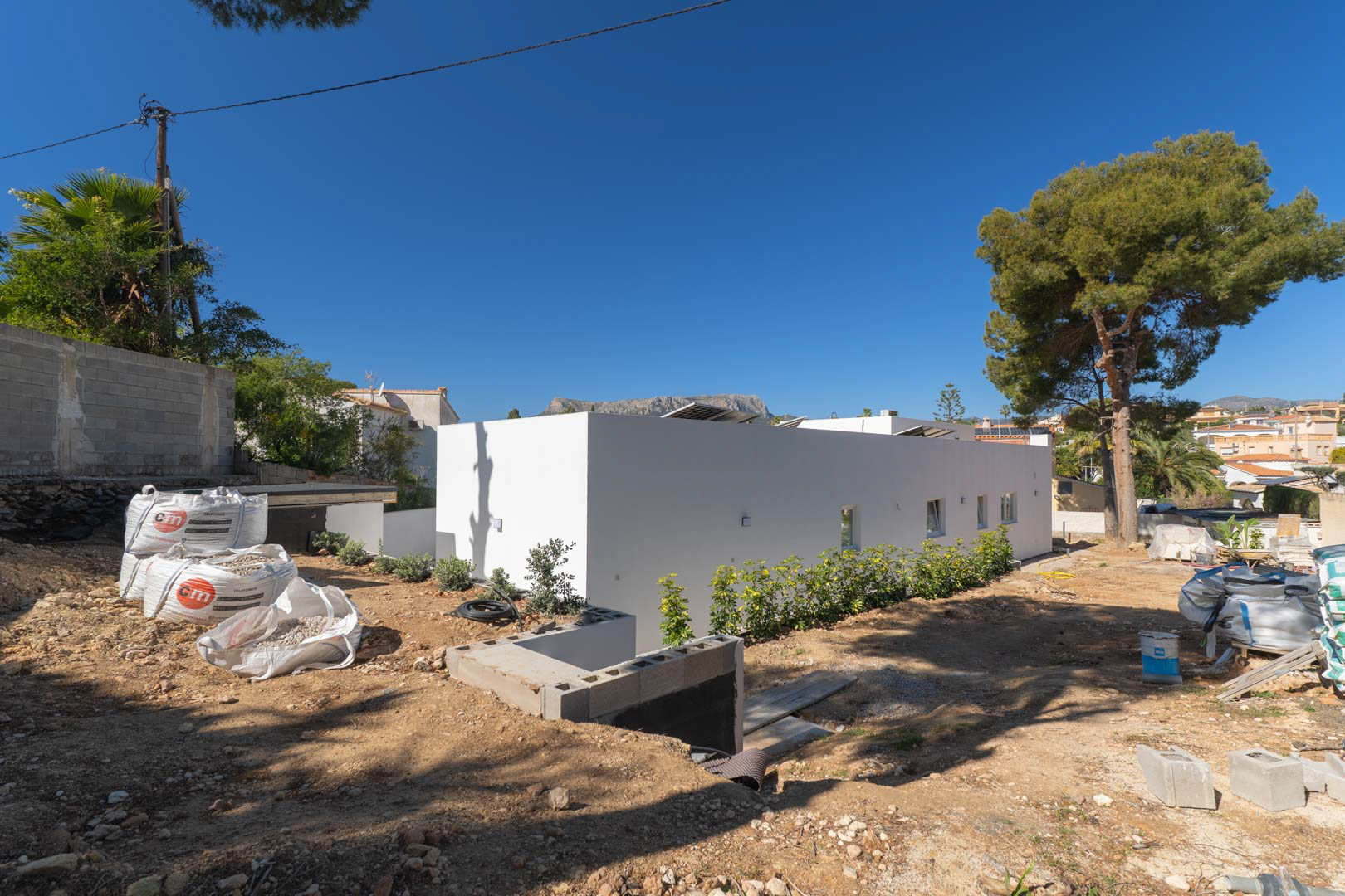 Villa minimaliste de plain-pied avec façade blanche et panneaux solaires. Le terrain extérieur est actuellement en phase de terrassement et d'aménagement paysager.