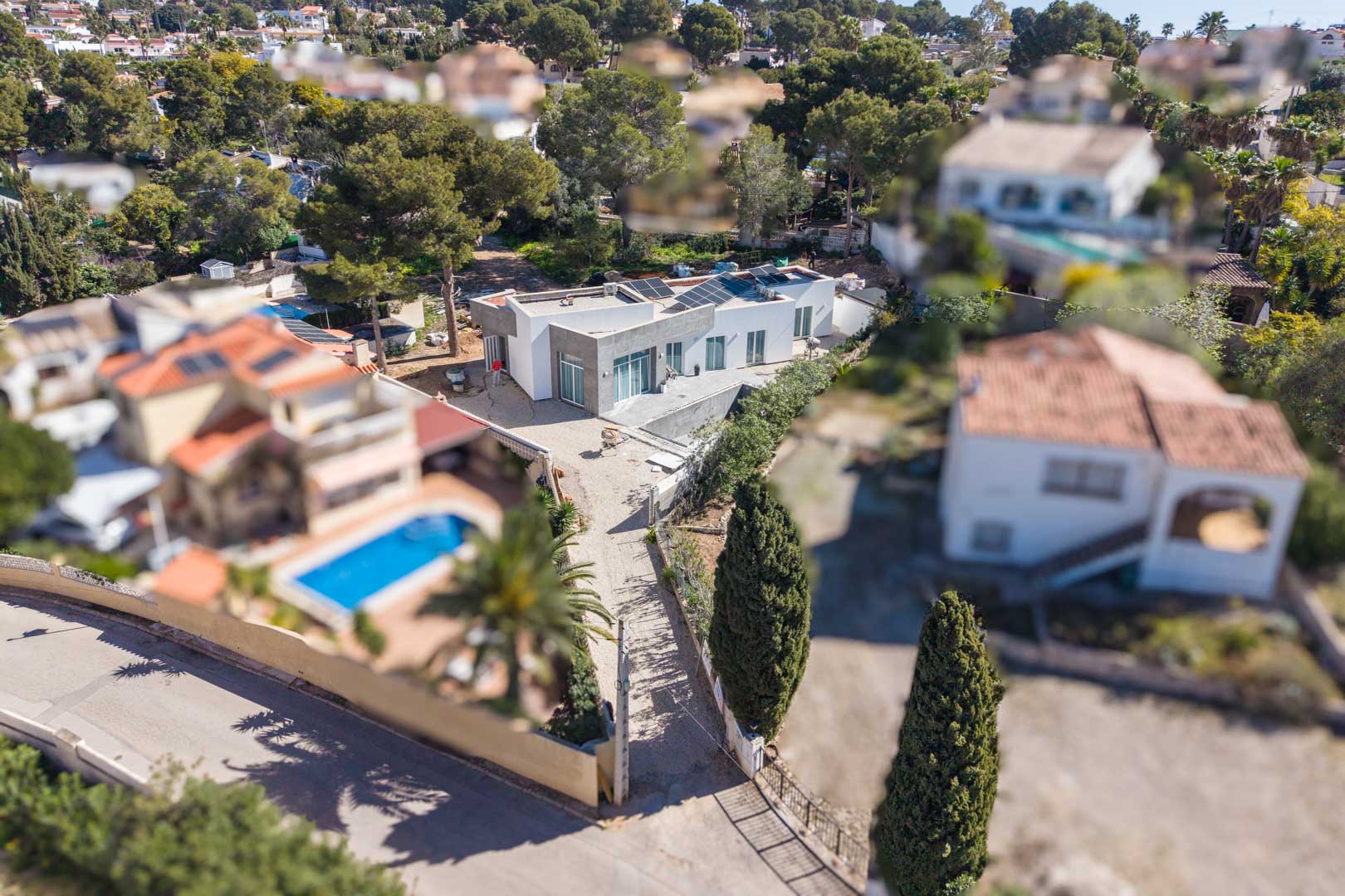 Vue aérienne de la villa minimaliste avec panneaux solaires sur le toit plat, illustrant le terrain en cours de finition au cœur d'un quartier résidentiel arboré.