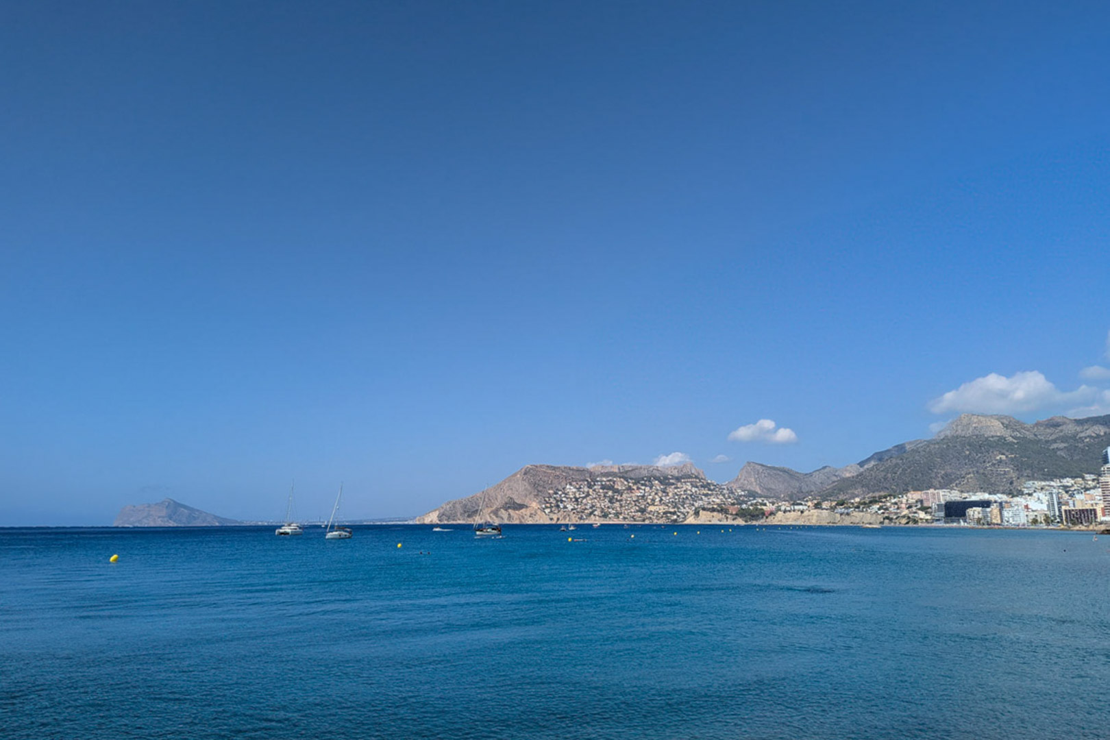 Vue panoramique sur la mer Méditerranée depuis la côte de Calpe, avec des voiliers et le relief montagneux de la Costa Blanca sous un ciel dégagé.