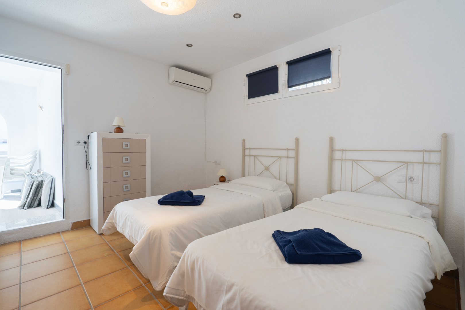 Chambre avec deux lits simples, sol en terre cuite et climatisation. Comprend un accès direct à la terrasse et une lumière naturelle abondante.