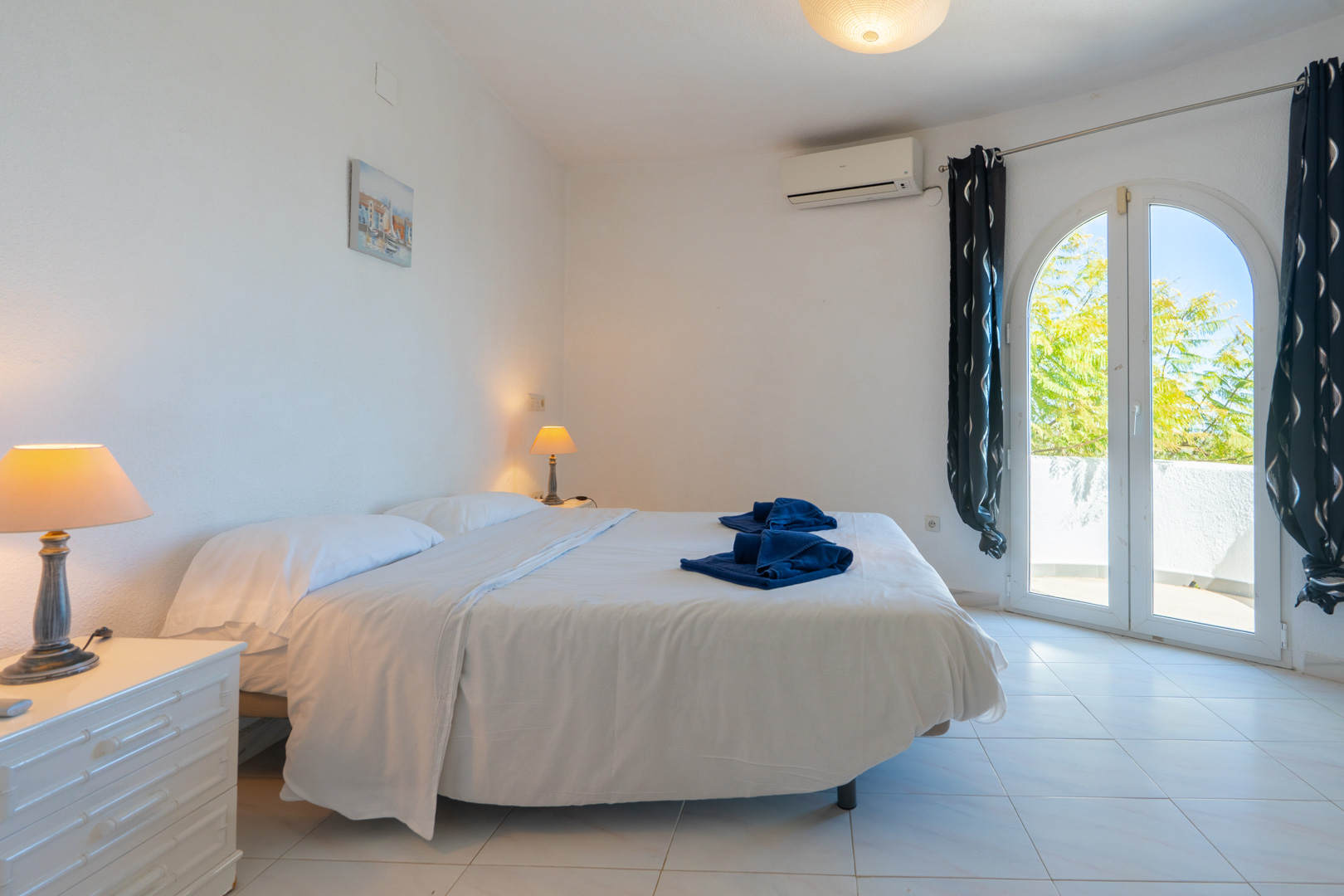 Chambre lumineuse avec lit double, climatisation individuelle et porte vitrée en arche offrant un accès direct à la terrasse.
