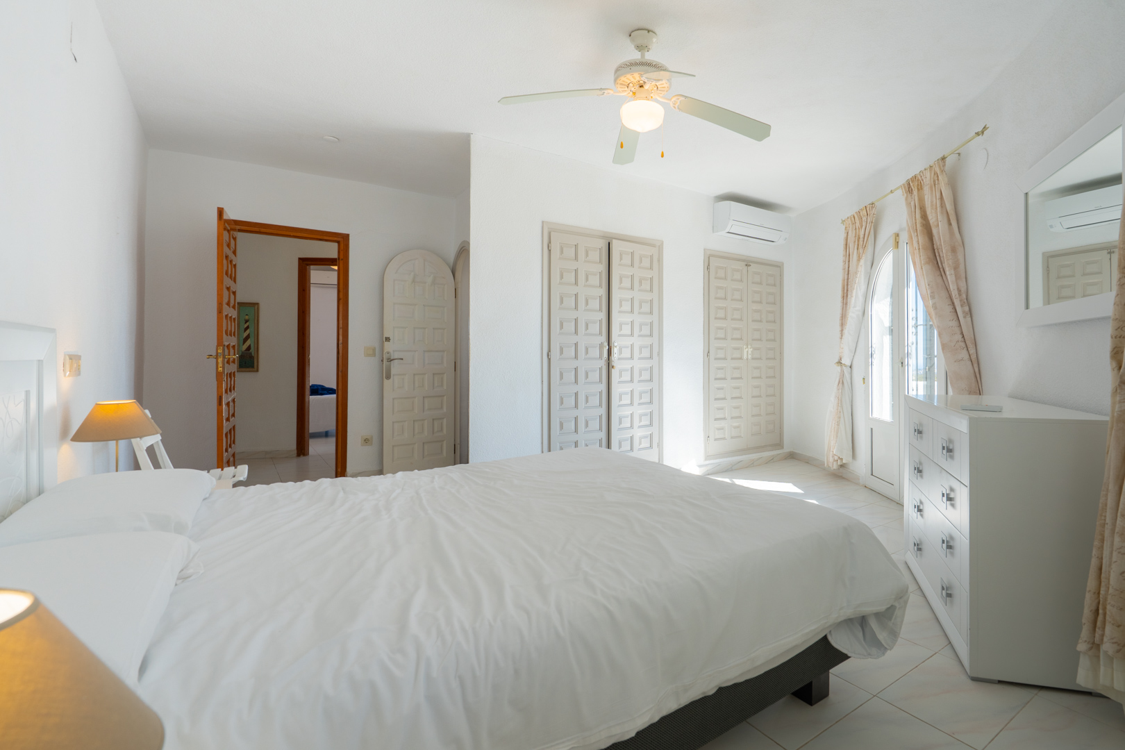 Chambre lumineuse avec placards intégrés de style traditionnel, climatisation, ventilateur de plafond et accès direct à l'extérieur par une porte vitrée.