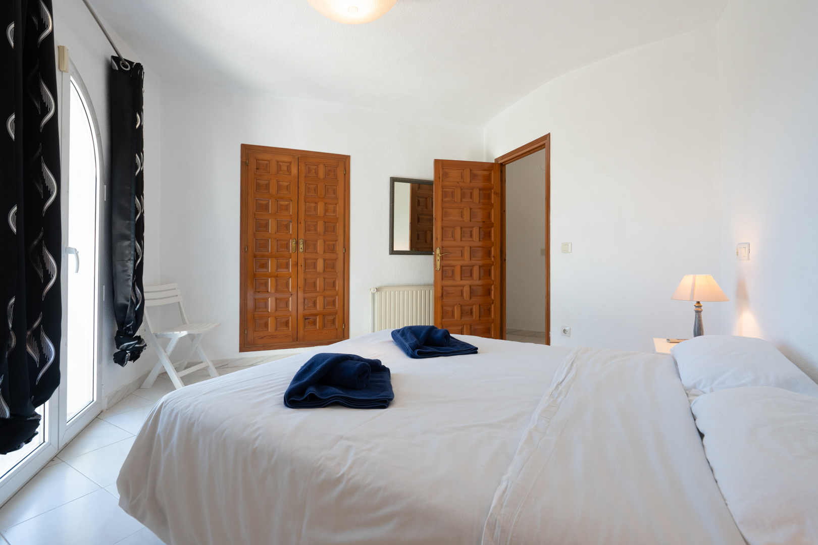 Chambre lumineuse avec placards intégrés en bois traditionnel, porte vitrée en arc offrant un accès extérieur et sol en carrelage clair.