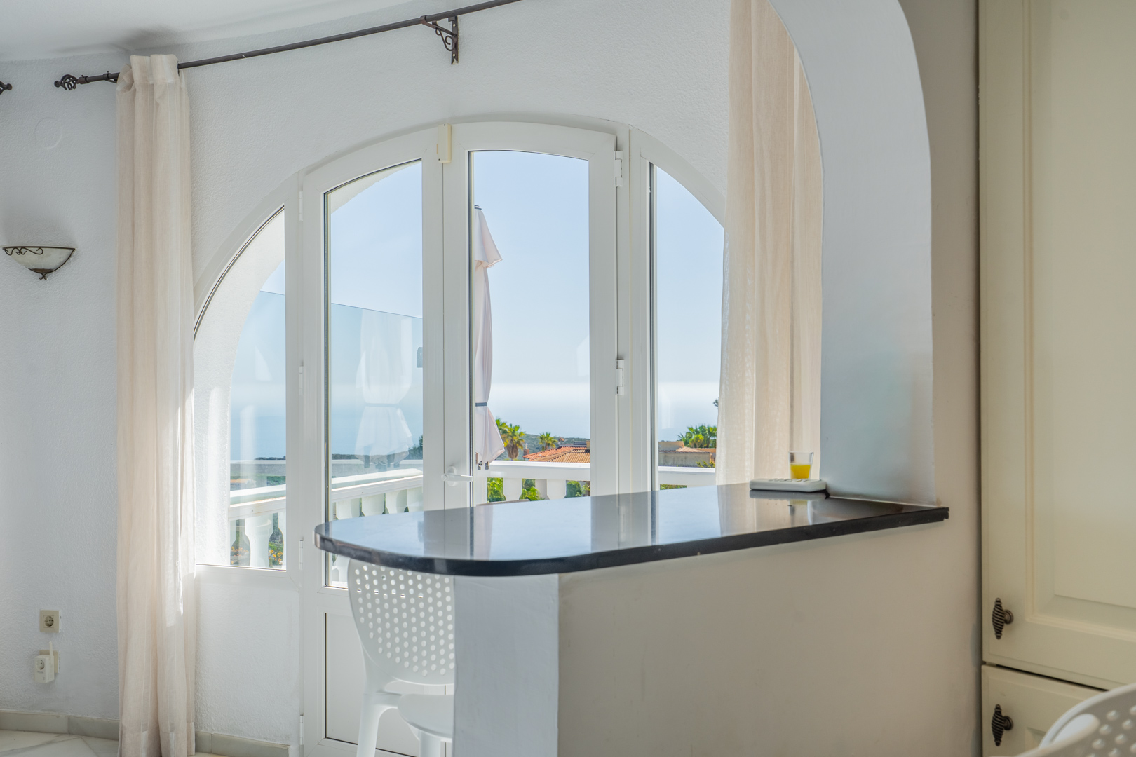 Comptoir de cuisine en granit sombre sous une arche, offrant une vue sur la mer à travers de grandes fenêtres cintrées menant à la terrasse.