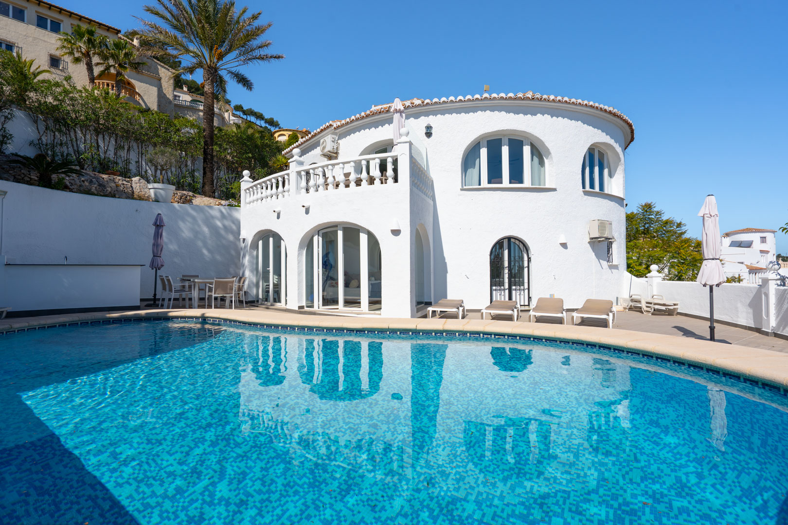 Extérieur de la villa avec piscine privée, terrasse et naya vitrée. La façade blanche présente des fenêtres cintrées et des balustrades de style traditionnel.