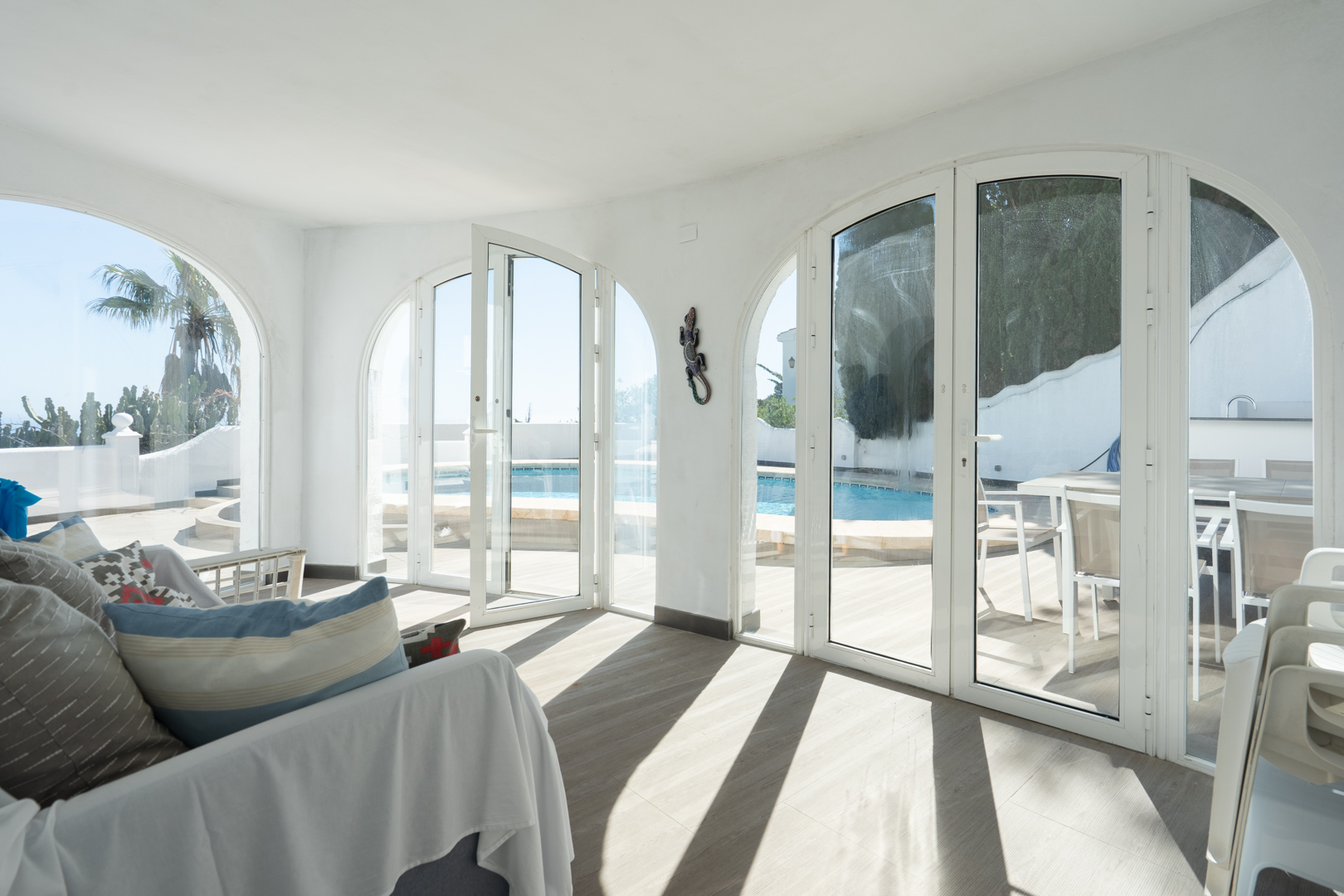 Naya vitrée avec de grandes portes en arc offrant un accès direct à la terrasse de la piscine et à l'espace de repas extérieur.