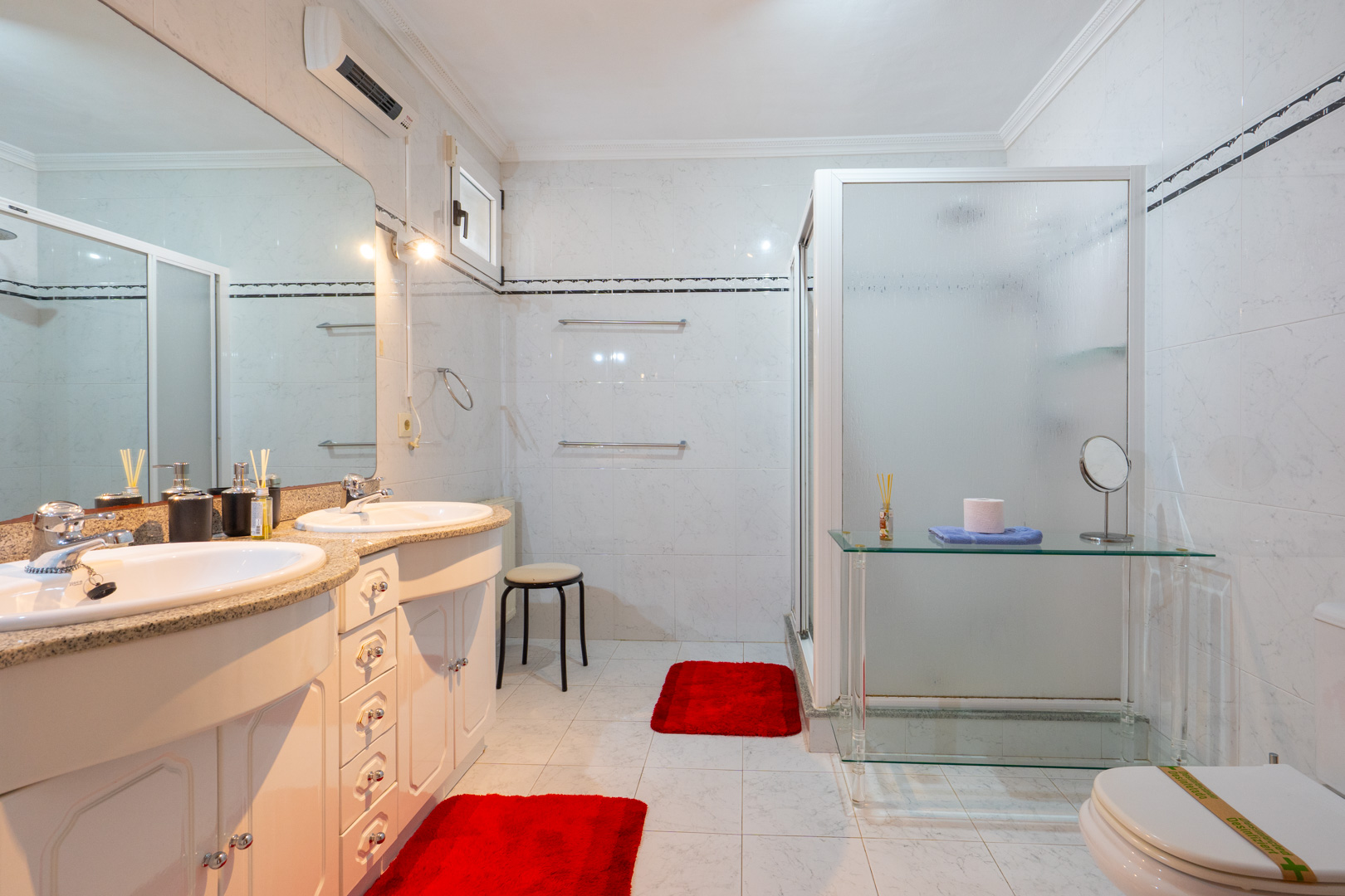 Salle de bain avec double vasque, plan de travail en granit et rangements blancs. Elle dispose d'une douche avec paroi dépolie et climatisation réversible.