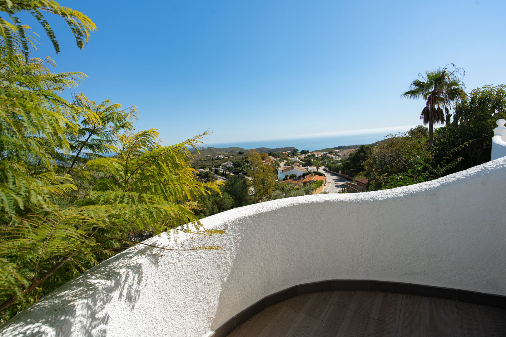 Terrasse avec un mur incurvé en crépi blanc et sol en grès, offrant une vue dégagée sur la mer Méditerranée et la végétation environnante de Cumbre del Sol.