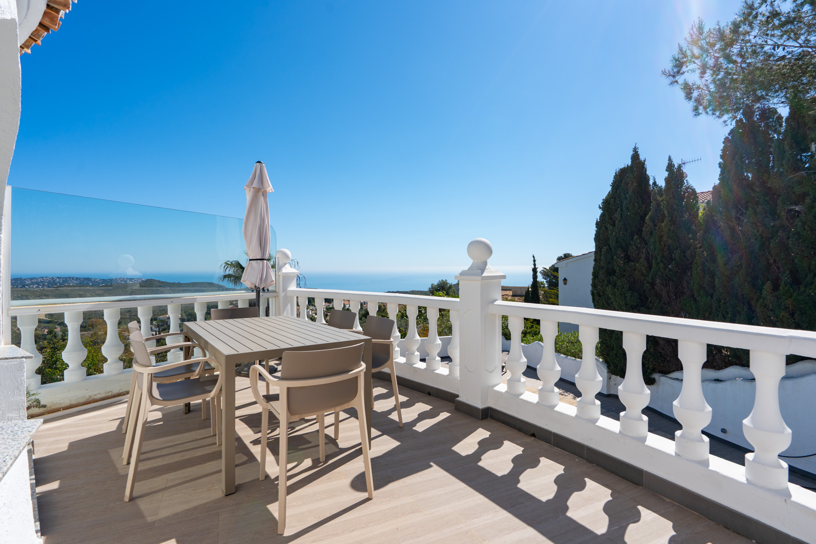 Terrasse supérieure avec balustrade blanche, mobilier de salle à manger moderne et vue panoramique sur la mer Méditerranée et le parc naturel.
