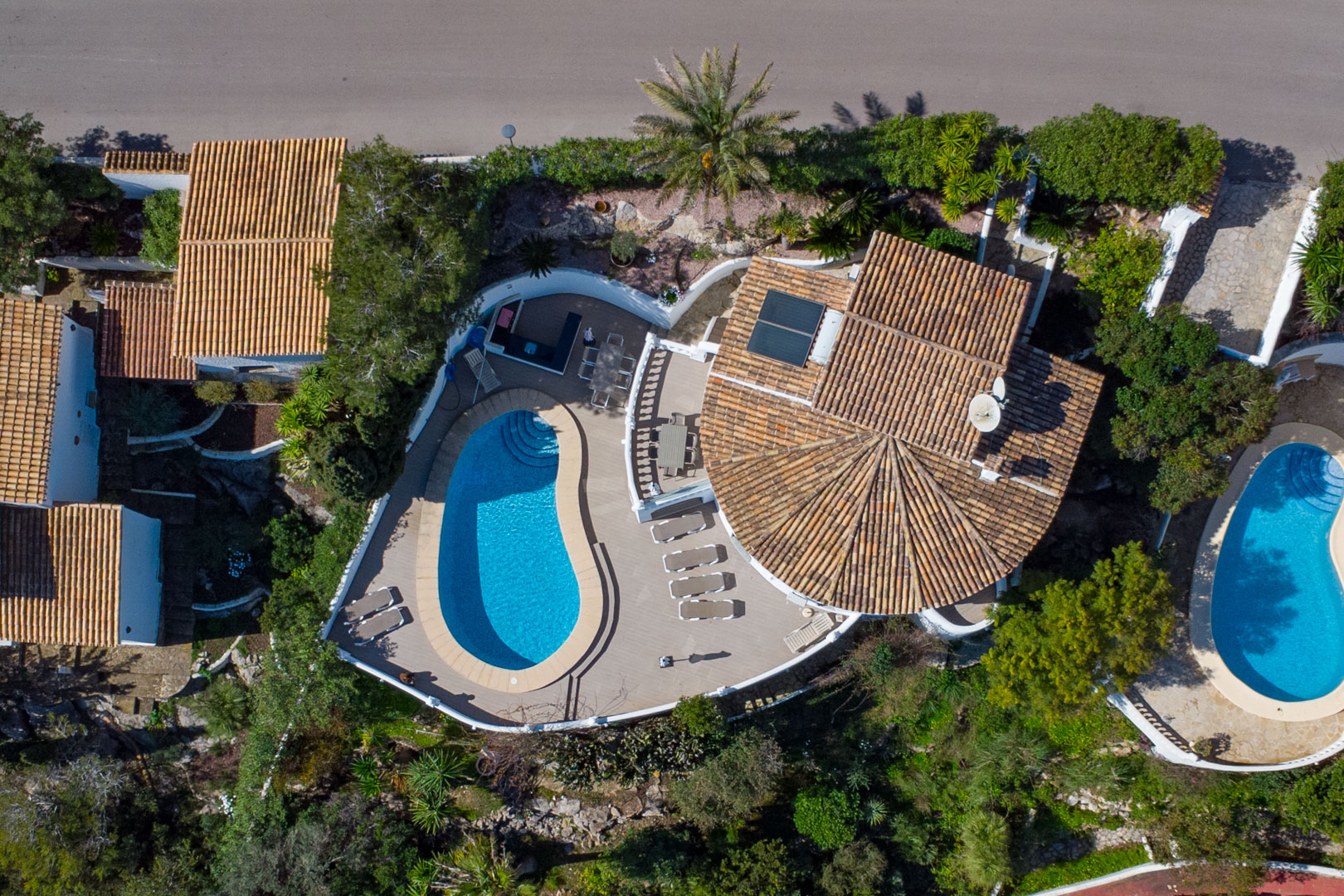 Vue aérienne de la propriété mettant en valeur la piscine incurvée, la grande terrasse avec salle à manger extérieure et le toit en tuiles avec panneaux solaires.