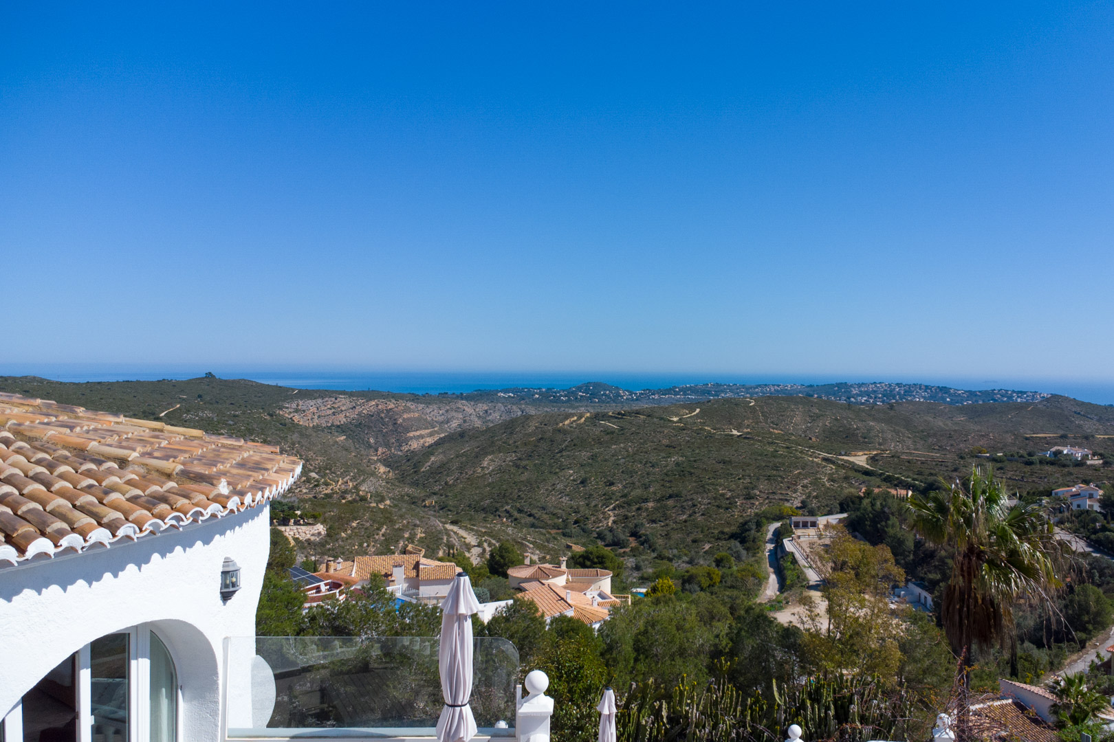 Vue panoramique depuis la villa sur le parc naturel de la Granadella et la mer Méditerranée, mettant en valeur l'architecture traditionnelle aux toits de tuiles.