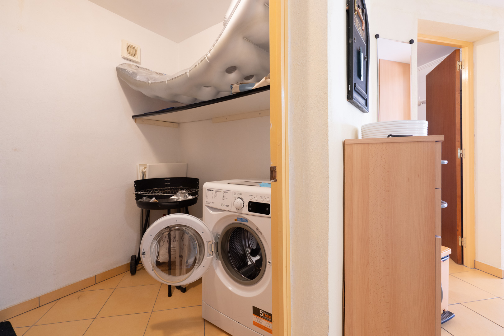 Buanderie fonctionnelle équipée d'un lave-linge à chargement frontal, d'une étagère de rangement et d'un sol en carrelage clair.