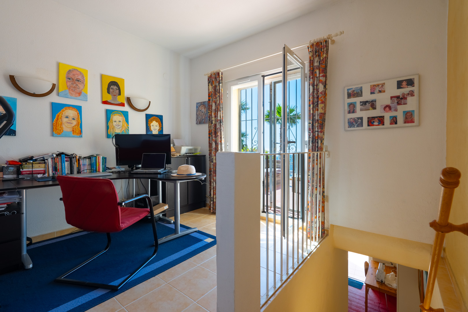 Bureau lumineux avec bureau d'angle, chaise rouge et accès terrasse. L'espace comprend un sol en grès et l'escalier menant au niveau inférieur.