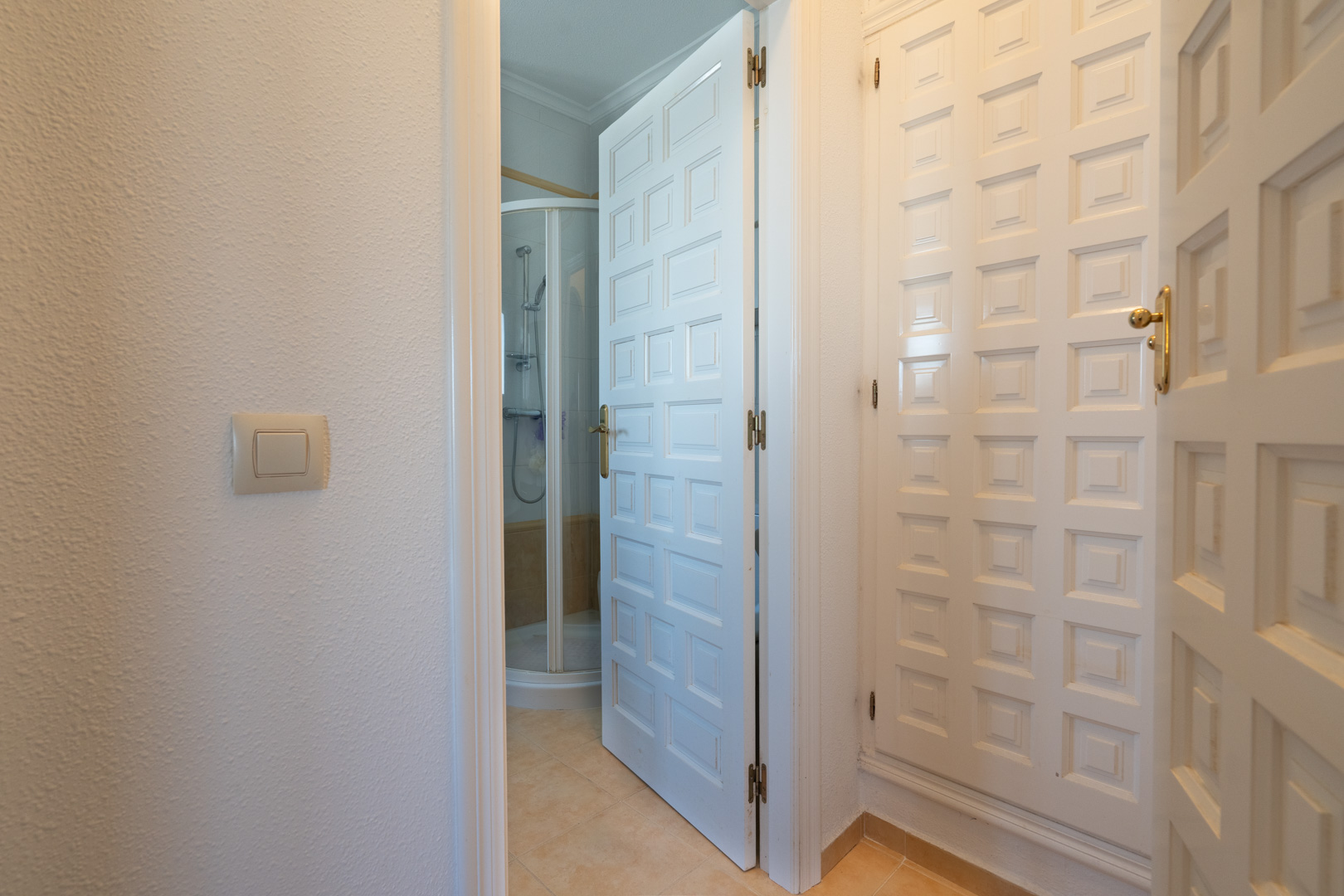 Couloir avec placards intégrés blancs et accès à une salle de bains disposant d'une cabine de douche d'angle et de carrelage clair.