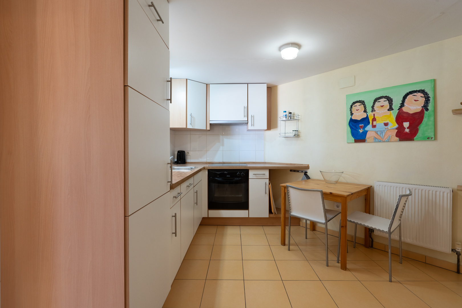 Cuisine fonctionnelle de l'appartement d'invités avec placards blancs, plans de travail en bois, coin repas compact et sol en carrelage beige.