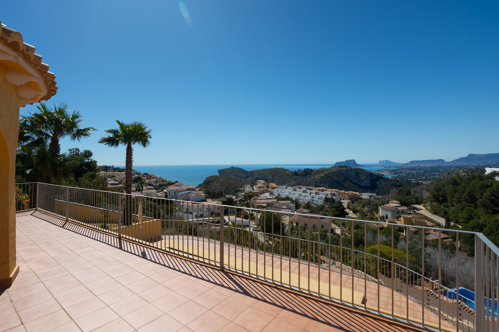 Grande terrasse ensoleillée avec garde-corps métallique offrant une vue panoramique sur la côte méditerranéenne, le Peñón de Ifach et les montagnes.