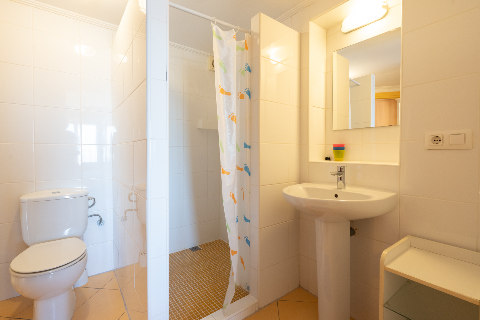 Salle de bains fonctionnelle avec carrelage blanc, douche à l'italienne avec rideau, lavabo sur colonne et finitions classiques.