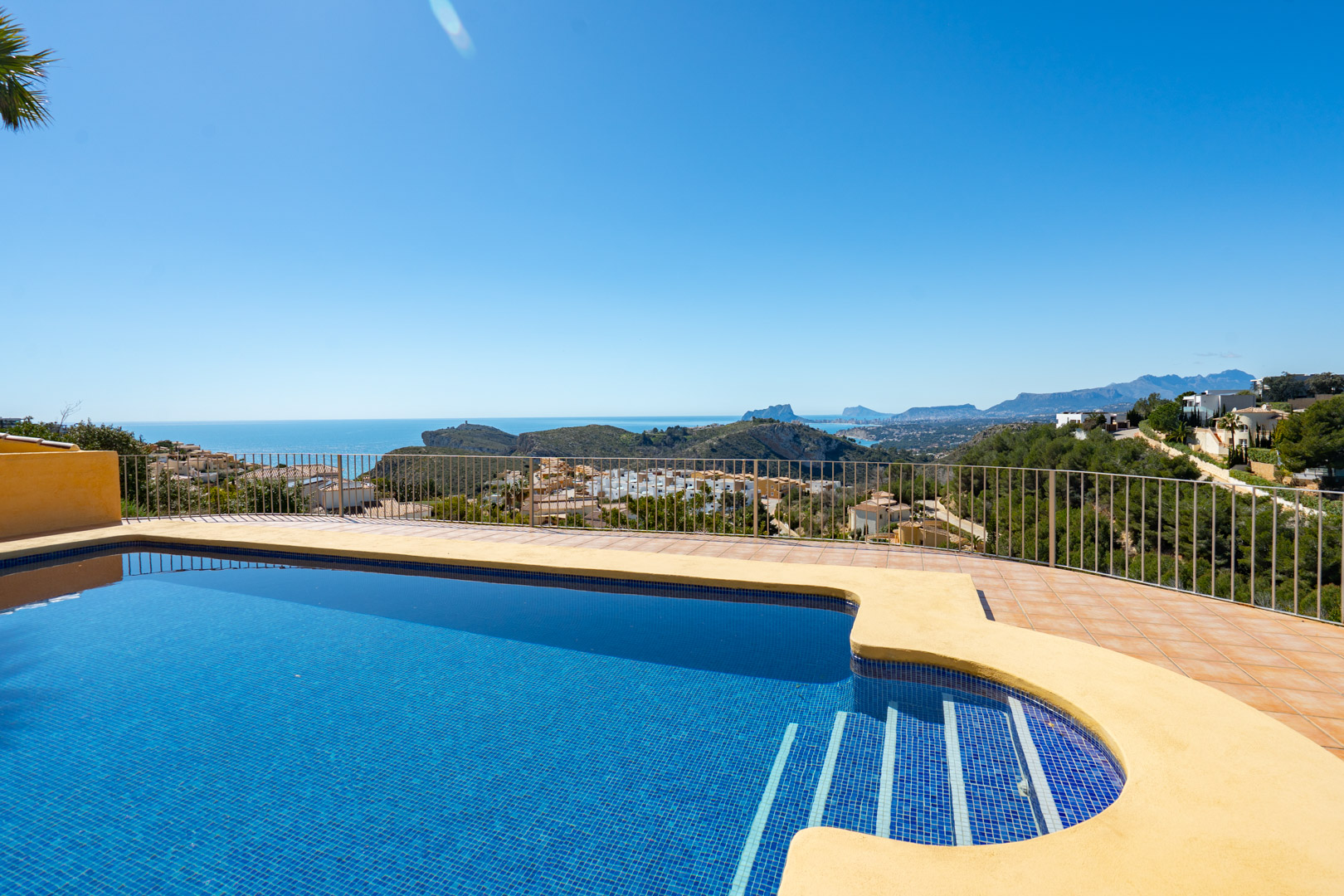Terrasse avec piscine en mosaïque bleue offrant une vue panoramique sur la côte méditerranéenne, le Peñón de Ifach et les montagnes environnantes.