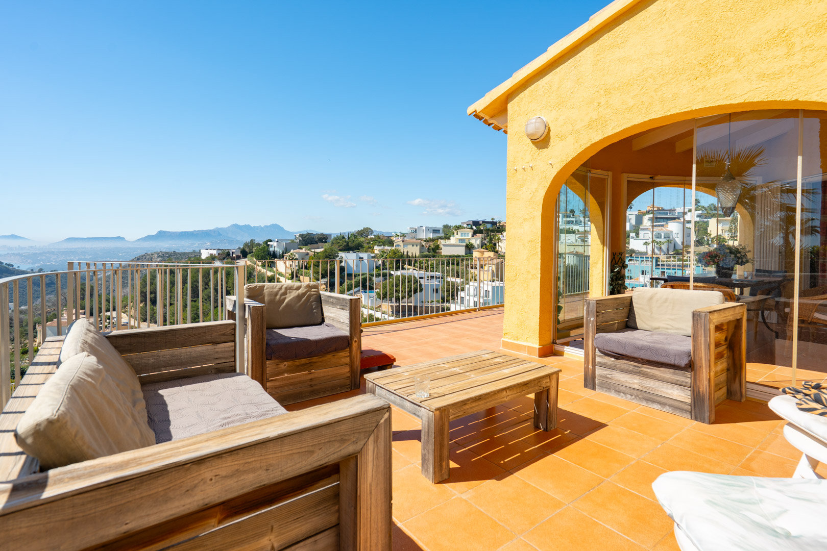 Terrasse solarium avec mobilier en bois rustique, carrelage en terre cuite et vue panoramique sur la côte et la Sierra de Bernia.