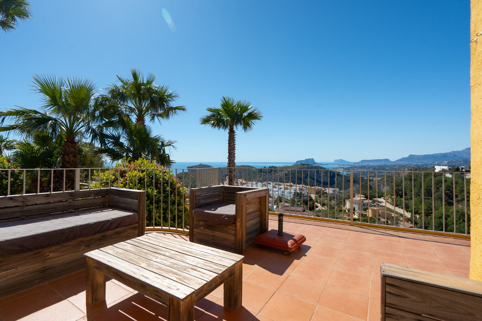 Terrasse solarium avec mobilier en bois rustique offrant une vue panoramique sur la mer Méditerranée, le Peñón de Ifach et la côte de Calpe.