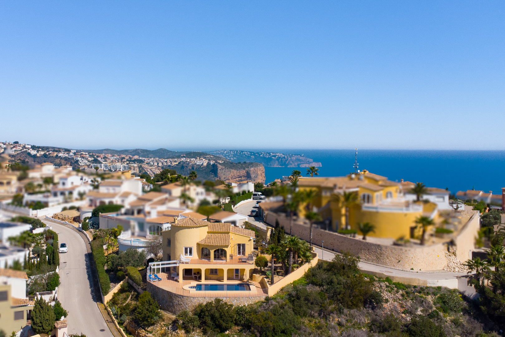 Vue aérienne de la villa à façade jaune, mettant en valeur sa piscine privée et ses terrasses avec vue panoramique sur la mer Méditerranée et le Cap d’Or.