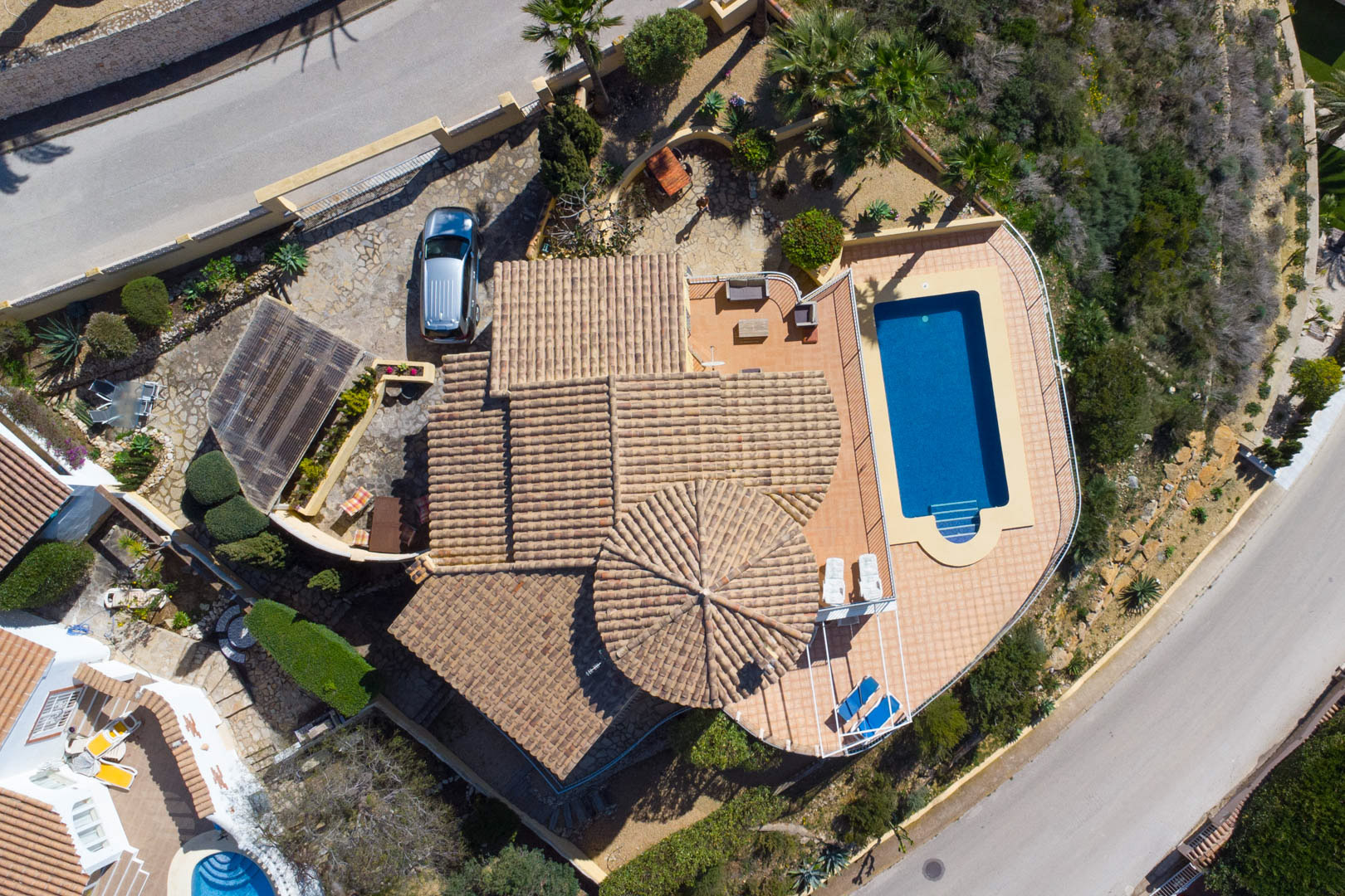 Vue aérienne de la villa soulignant l'architecture traditionnelle des toits, la piscine rectangulaire avec terrasse et l'allée pavée menant au carport privé.