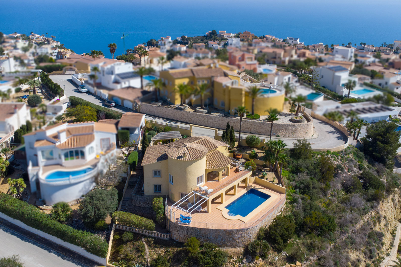Vue aérienne de la villa traditionnelle avec sa façade jaune, sa tour circulaire et sa piscine privée entourée d'une grande terrasse face à la mer.