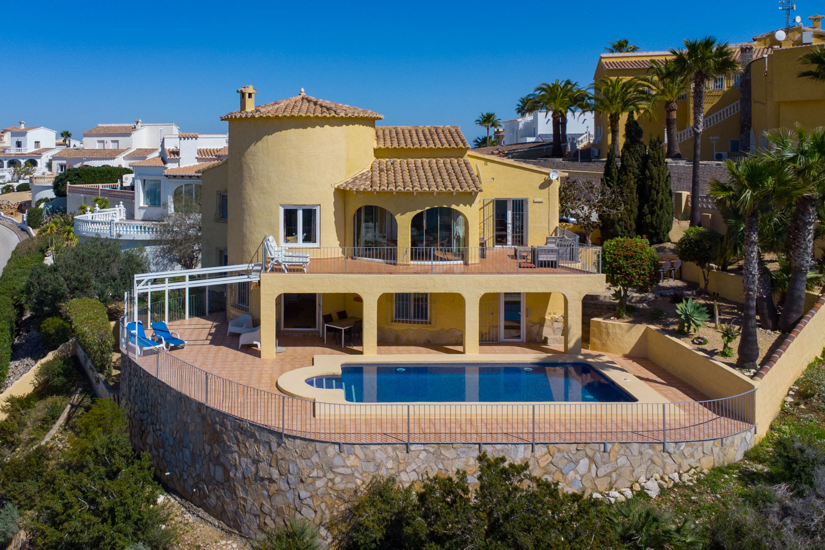 Vue extérieure de la villa avec piscine privée, terrasses en terre cuite sur deux niveaux et un imposant mur de soutènement en pierre naturelle.